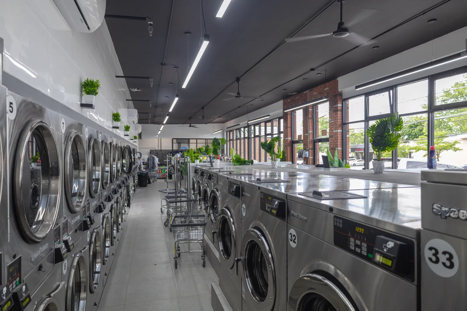 Main aisle with stacked dryers, large washers and laundry carts inside Neatly, 1936 Victory Blvd